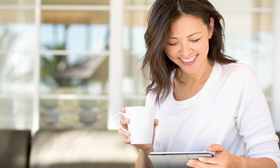 Young woman holding mug while reading tablet