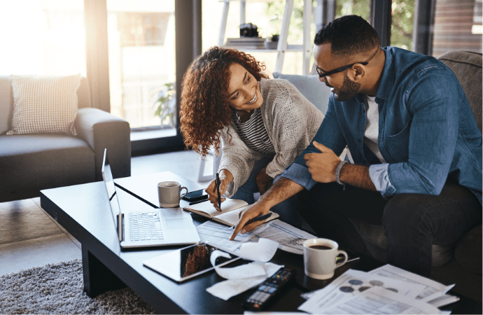 Two people discussing finances at a coffee table covered with books and a laptop