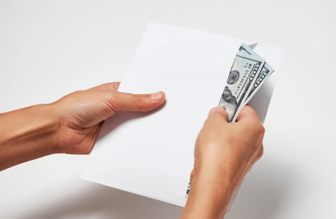 Hands putting a stack of dollar bills into a white envelope