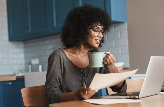 Young woman drinking coffee while looking at her laptop.