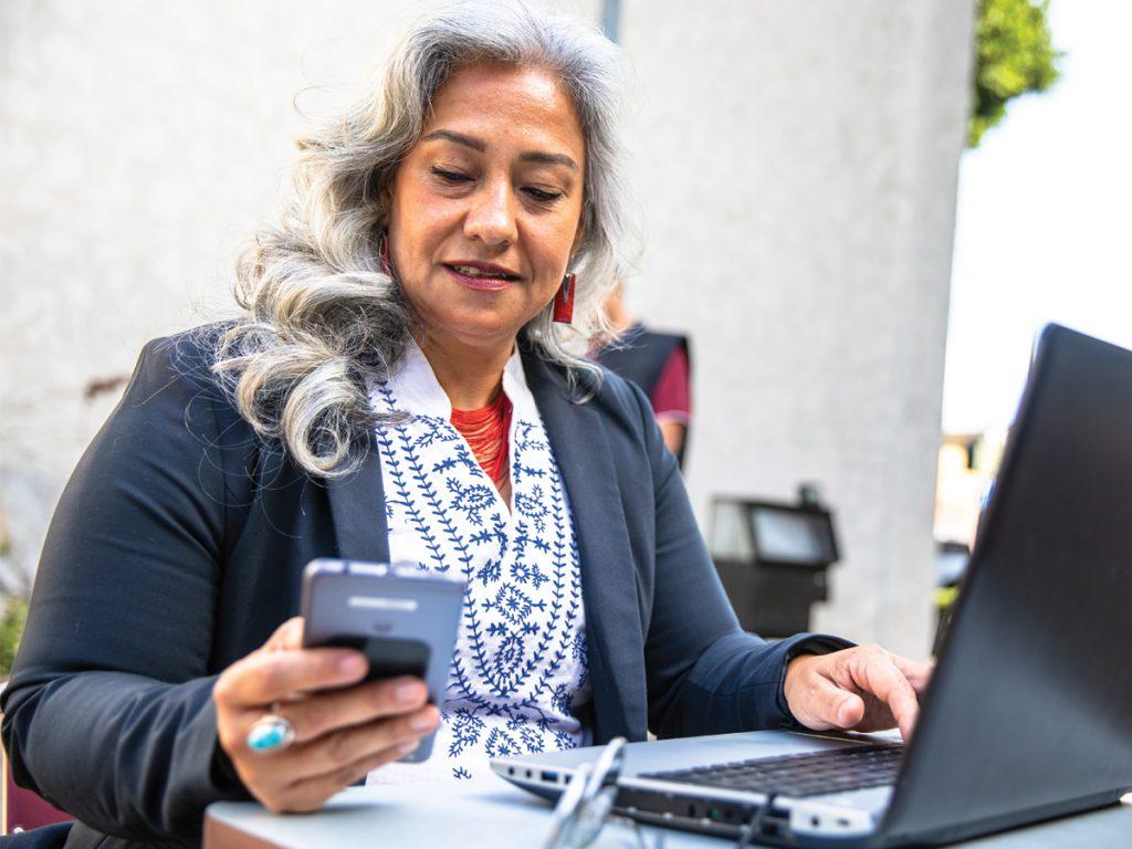 Woman checking her phone while working on a laptop.