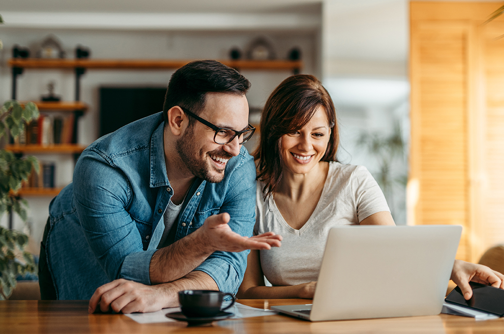Portrait of a smiling couple looking at laptop together at cozy home office.