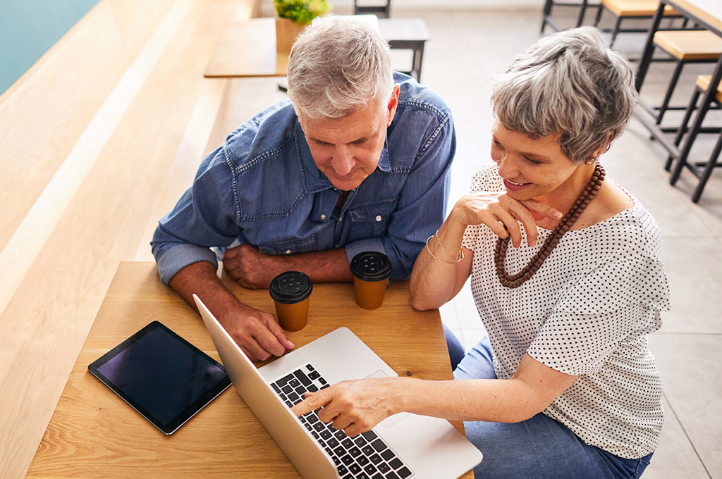 High angle of a mature senior couple sitting having coffee in a cafe and talking together over a laptop